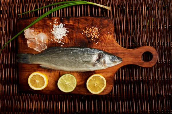 Limon dilimleri ve soğan bir kesme tahtası deniz tuzu yanında yatan Levrek Marine