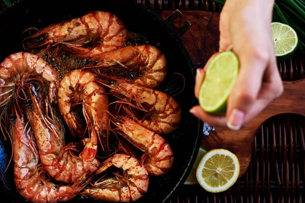 Roasted tiger prawns on a hot cast iron  fried in butter with lime and herbs in the restaurant. Process of cooking. Shrimp on the grill.  Exquisite dish of seafood. Food background. Selective focus.
