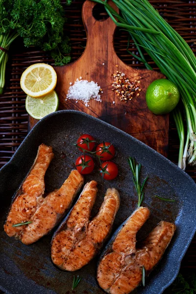 Konuklar için somon yemek biftek pişirmek için karım bekler, Balık biftek ızgara Pan rosemary ile ve domates, bir tava ile ahşap bir gemide kızarmış balık koymak