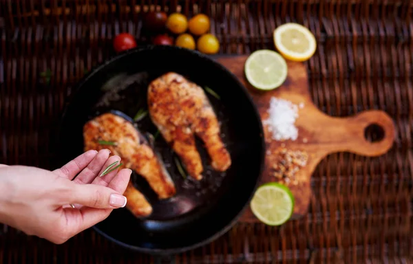 Girl salts Two red fish steak fried in a frying pan for two persons, is a pan on a wooden board close tomatoes and slices of lemon and lime