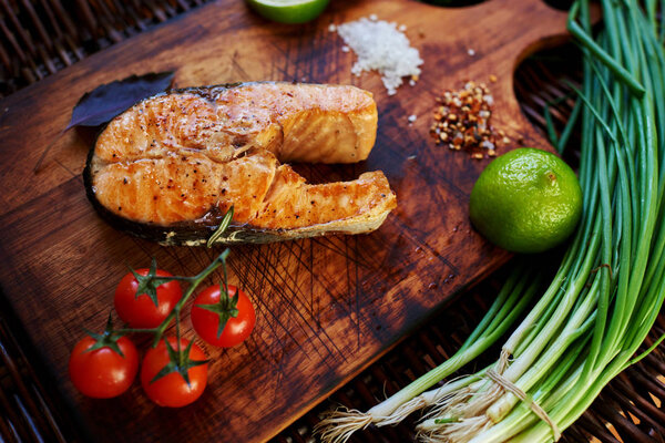 ook restaurant cooked a salmon steak on the grill and served with him a piece of lemon, onion, few tomatoes. Fish lying on a wooden surface, close to her small tomatoes on a branch