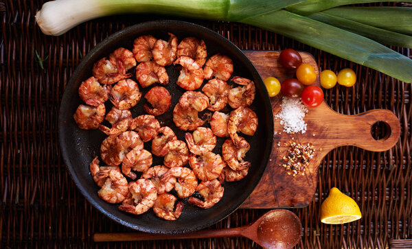 Shrimp fried in soy sauce with garlic in olive oil first press, served in a cast iron skillet, poured lemon juice, Cherry tomatoes yellow and red complement the composition with shrimp and parey