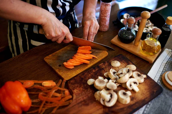 家庭主妇在条纹围裙削减蔬菜 将使晚餐 — 图库照片
