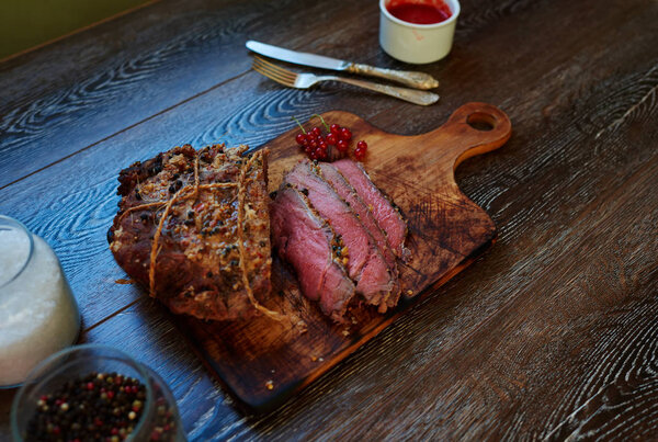 Appetizing veal tenderloin baked in the oven until  blue rare, the cook served on a cutting board, standing next to the sauce to the meat of wild berries