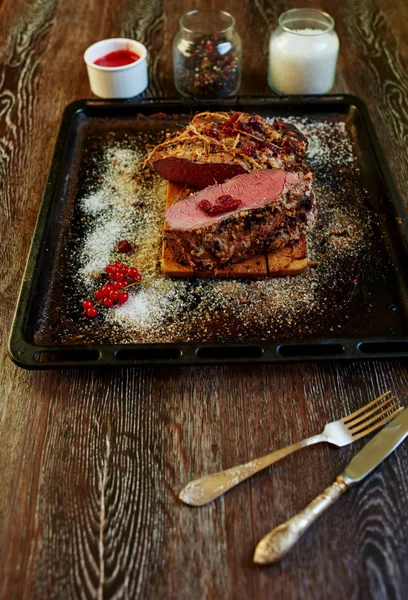 Üstten görünüm masanın üzerine kuzu fırın tepsisi yanındaki ekşi yabani çilek ilavesi ile baharatlı sosu yanında duran, büyük bir parçası olan bir pan olmasıdır gümüş çatal bıçak takımı