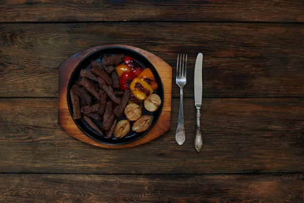 Hangi cool taze hazırlanmış kuzu eti ve bir ızgara, kızarmış sebze yalan yanında gümüş çatal bıçak takımı bir düz dökme demir tava üzerinde karanlık bir ahşap tablodur