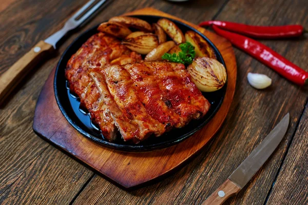 在桌子上是铸铁锅与美味的肉 烤至金黄 用木柄谎言附近刀叉餐具 — 图库照片