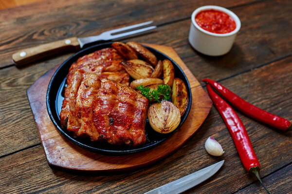 Cook in the oven fried pork ribs with vegetables served on a wooden platter, sauce prepared with tomatoes and hot chile ertsa