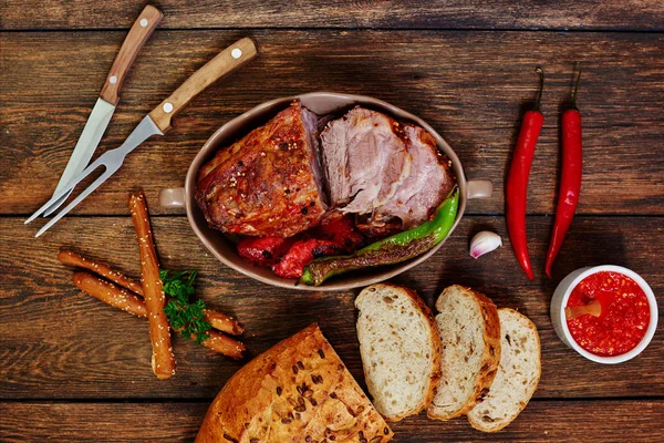 Baked sliced pork loin in ceramic form with fork, knife and homemade rustic bread on dark rustic background. Roasted pork served with grilled vegetables and tomato sauce. Cozy village dinner