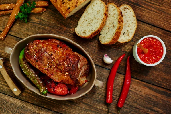 Baked pork loin  in ceramic form with fork, knife and homemade rustic bread on dark rustic background. Roasted pork served with grilled vegetables and tomato sauce. Cozy village dinner