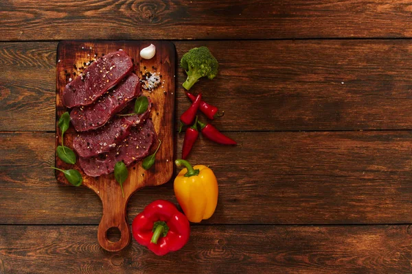 Çeşniler koyu arka plan üzerinde ile çiğ taze et ahşap tahta üzerinde. Biber biber, ot, tuz ve karabiber. Biftek hazır. Kopya alanı ile üstten görünüm.