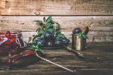 Bir kavanozda erik sosu ve bir masada mavi olgun erik. Sağlıklı, organik, ev yapımı yiyecekler. Tonlu görüntü.