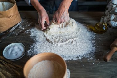 Kadın elleri pizza için hamur yapıyor. Fırıncı mutfak masasında taze çiğ hamur yoğurunuyor. Doğa kavramı, İtalya, gıda, diyet ve biyo. Düşük tuş atış, ellere yakın, masanın etrafında bazı malzemeler.
