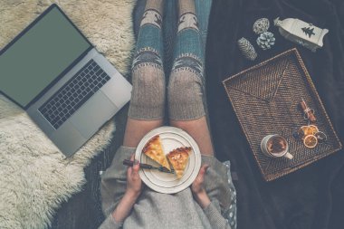 Kız evde rahatlatıcı noel pastası plaka tutan, kakao içme, dizüstü bilgisayar kullanarak. Kısa mesaj veya reklam için kopyalama alanı ile boş ekran. Sıcak rahat ev noel ruh hali. Yumuşak renkler.