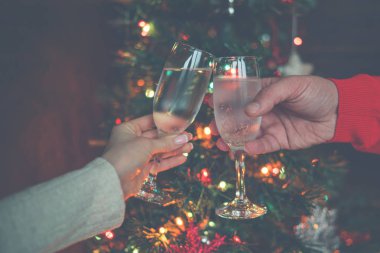 Noel ağacı parlayan ışıklara karşı kadeh kaldıran iki kadeh şampanya. Tatil ve birliktelik bir aile Noel ve Happy New Year. Parti zamanı. Şampanyalı bir çift. Seçici odaklama.