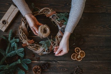 Noel kompozisyonu. Koyu ahşap rustik masaüzerinde el yapımı noel çelengi yapan kadın. Mutlu tatiller için hazırlık kavramı. Şenlikli iç dekor. Üst görünüm, kopyalama alanı ile düz yatıyordu.