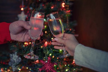 Noel ağacı parlayan ışıklara karşı kadeh kaldıran iki kadeh şampanya. Tatil ve birliktelik bir aile Noel ve Happy New Year. Parti zamanı. Şampanyalı bir çift. Seçici odaklama.
