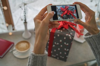 Genç bir kadın, blogcu Noel tatili için hazırlanıyor ve akıllı telefonda fotoğraf çekiyor. Sosyal ağlarda cep telefonu tutan ve sohbet eden bir kadının elleri. Görüntü tonlaması. Seçici odak.