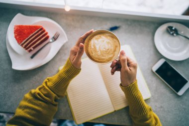Kafede pasta ile kadın elinde kapuçino fincan. Sıcak içecek. Sonbahar veya kış aylarında rahat kahve dükkanı atmosferi. Sonbahar veya kış dinlenmek kavramı. Sıcak vintage tonlama. Seçici odaklama.
