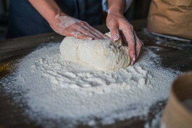 Kadın elleri pizza için hamur yapıyor. Fırıncı mutfak masasında taze çiğ hamur yoğurunuyor. Doğa kavramı, İtalya, gıda, diyet ve biyo. Düşük tuş atış, ellere yakın, masanın etrafında bazı malzemeler.