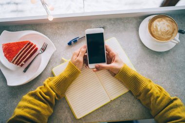 Akıllı telefon ve kağıt defter üzerinde çalışan genç bir kadın ya da öğrenci, kafede akıllı telefon kullanan genç bir kadın, online çalışma konsepti. Bir kadının ellerini kapayarak not alın. Tonu ayarlanmış resim.