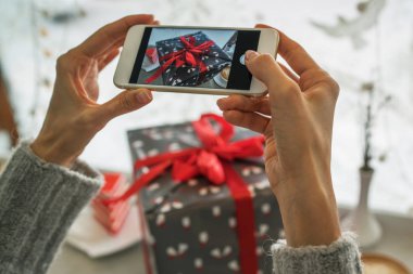 Genç bir kadın, blogcu Noel tatili için hazırlanıyor ve akıllı telefonda fotoğraf çekiyor. Sosyal ağlarda cep telefonu tutan ve sohbet eden bir kadının elleri. Görüntü tonlaması. Seçici odak.