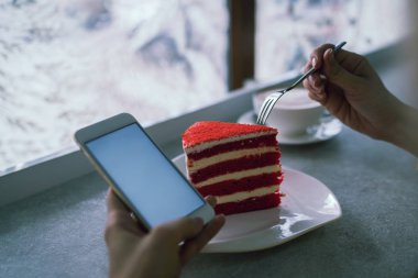 Kahve dükkanında sıcak kahve fincanı ve kek ile boş beyaz ekran ile beyaz cep telefonu tutan ellerin kırpılmış görüntü. Ücretsiz wifi bağlı akıllı telefon gelen sms mesajı okuma Kadın.