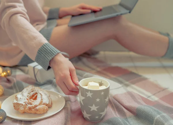 Winter hot drinks. Close up cup of coffee or hot chocolate. Blurred image womam in warm pink sweater with laptop, home comfort and relax. Christmas holidays, hot drinks and people concept.