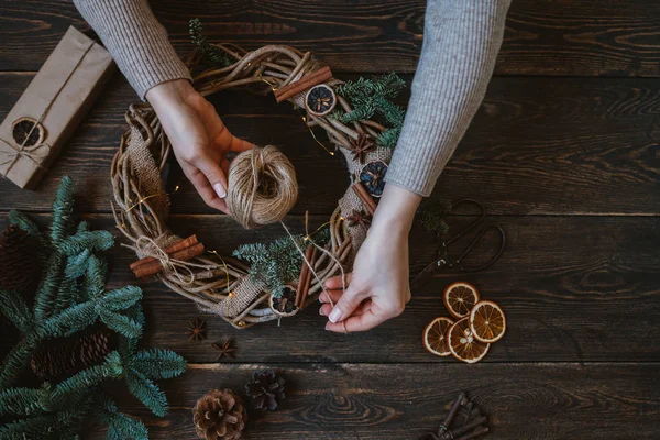 Noel kompozisyonu. Koyu ahşap rustik masaüzerinde el yapımı noel çelengi yapan kadın. Mutlu tatiller için hazırlık kavramı. Şenlikli iç dekor. Üst görünüm, kopyalama alanı ile düz yatıyordu.