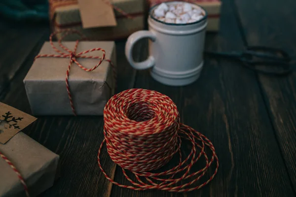 Christmas background with cup coffee and gift boxes on rustic wooden board. Presents, decoration and twine ribbon. Luxury New Year or Christmas gift. Preparation for the holidays. Toned image.