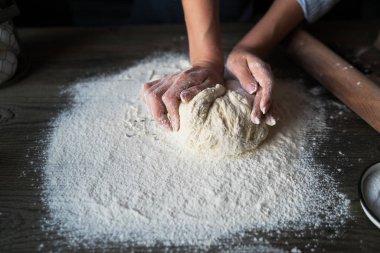 Doğal ışık ile ahşap bir yüzeyüzerinde ekmek veya pizza için hamur. Koyu ahşap arka plan üzerinde Eller pişirme hamuru. Gıda konsepti. Seçici odaklama.