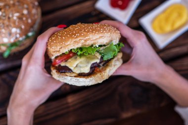 Çizburger tutan kadın. El ele tutuşan genç bir kız fast food burger, Amerikan yemeği. Köy tahtasında patates kızartması ve sığır burger. Seçici odaklanma. Kopyalama alanı olan ayarlanmış resim.
