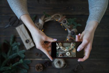 Noel dekorasyon akıllı telefon resimleri ile Eller. Genç kadın, blogcu evde tatil için hazırlanıyor ve akıllı telefonda fotoğraf yapıyor. Instagram blogger atölye konsepti. Tonlu görüntü.