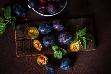 Kahverengi ahşap bir tahta üzerinde yaprakları ile taze olgun erik. Üst görünüm, tonda görüntü. Seçici odaklama.