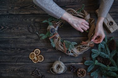 Noel kompozisyonu. Koyu ahşap rustik masaüzerinde el yapımı noel çelengi yapan kadın. Mutlu tatiller için hazırlık kavramı. Şenlikli iç dekor. Üst görünüm, kopyalama alanı ile düz yatıyordu.