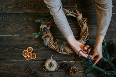 Noel kompozisyonu. Koyu ahşap rustik masaüzerinde el yapımı noel çelengi yapan kadın. Mutlu tatiller için hazırlık kavramı. Şenlikli iç dekor. Üst görünüm, kopyalama alanı ile düz yatıyordu.