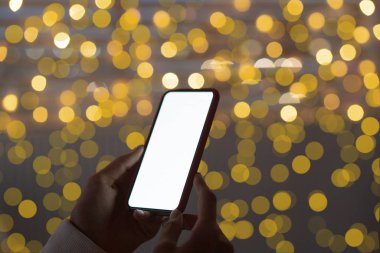 Sokakta cep telefonunu kullanan bir kadın, Noel gecesi lambası arka planı..