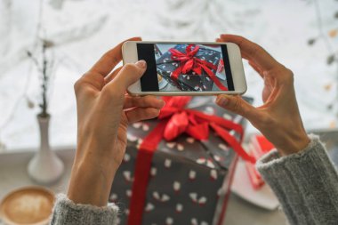 Genç bir kadın, blogcu Noel tatili için hazırlanıyor ve akıllı telefonda fotoğraf çekiyor. Sosyal ağlarda cep telefonu tutan ve sohbet eden bir kadının elleri. Görüntü tonlaması. Seçici odak.