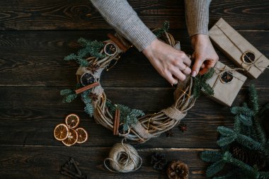 Noel kompozisyonu. Koyu ahşap rustik masaüzerinde el yapımı noel çelengi yapan kadın. Mutlu tatiller için hazırlık kavramı. Şenlikli iç dekor. Üst görünüm, kopyalama alanı ile düz yatıyordu.
