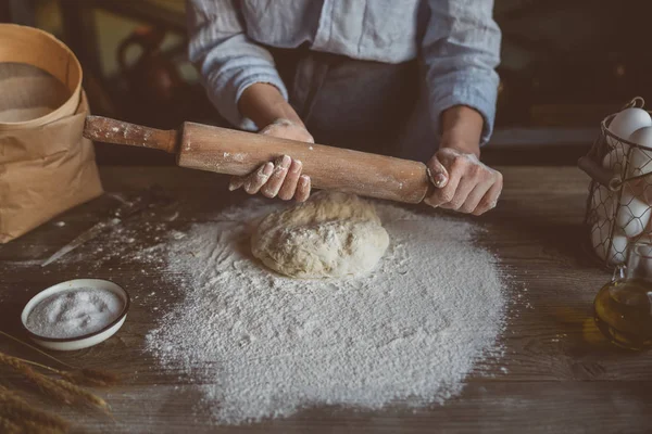 Woman kneading dough for pasta or pizza on table. Dough, flour with kitchen utensils on the old wooden table. Healthy, organic and vegetarian food. Food concept. Selective focus. Rustic style.