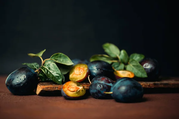 Garden plums on table. Close up of fresh plums with leaves. Summer or autumn harvest of plums. Toned image. Selective focus.