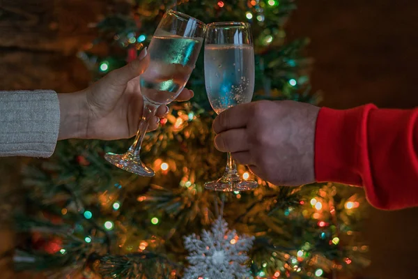 Cheers! Womam and man cheering with champagne flutes on the Christmas interior in the background. Holidays concept. Evening lights glowing. New Year celebration. Toned image. Selective focus.