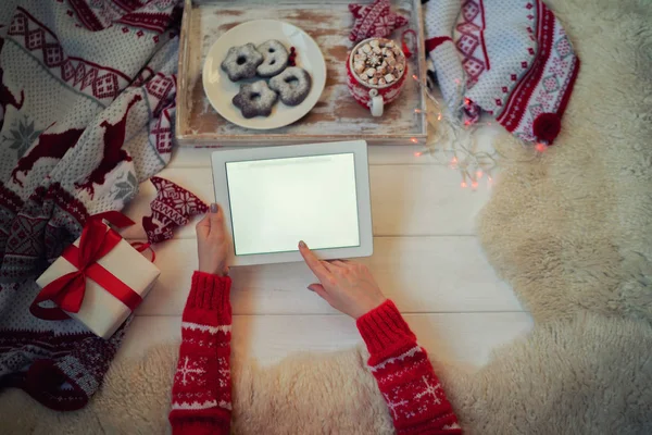 Young woman laying on knit blanket, relaxing, watching something on her tablet. Flat lay of seasonal home craft decor. Coffee or tea break for home relax. Winter or concept, warm homely scene.