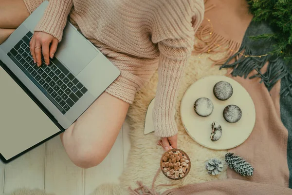 Workspace with laptop, girl\'s hands, cup hot chocolate, white vintage tray with cake, christmas decor on white background. Freelancer working place. Merry Christmas! Top view. Selective focus.