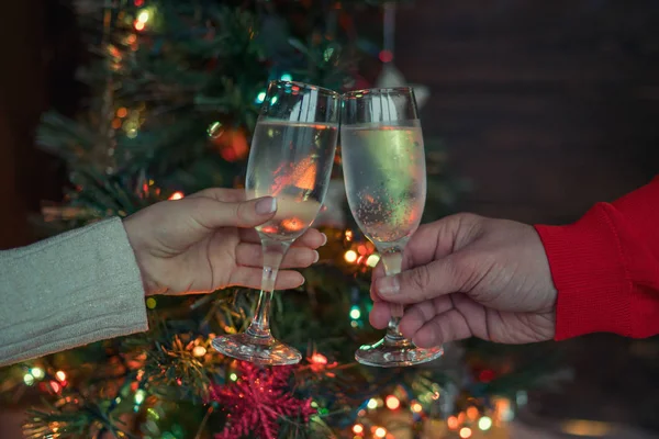 Christmas illuminations and champagne glasses. Hands of people with glasses of champagne, celebrating and toasting in honor of the Christmas and Happy New Year. Couple cheering with champagne flutes.