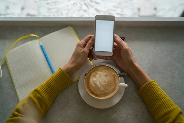 Young woman or student working on smart phone and writing on paper notebook, young woman using smart phone at coffee shop, online working concept. Close up of woman\'s hands making notes. Toned image.