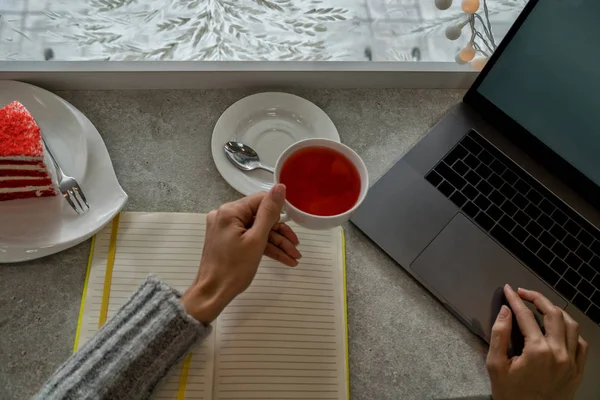 Entrepreneur with a laptop relaxing in a coffee shop enjoying a cup of fruit tea. Hot tea cup on a frosty winter window background. Cozy coffee shop atmosphere in winter. Selective focus.