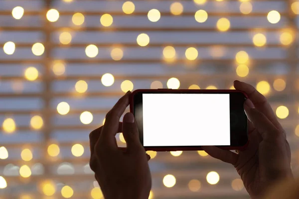 Black mobile phone in woman hand close up. Christmas greeting on phone. Christmas bokeh lights in background.