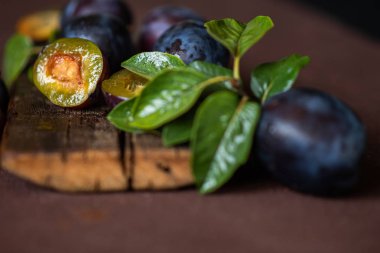 Koyu ahşap arka planda damla erik. Mavi erik meyvesinin yarısı ve tamamı. Yaprakları ile birçok güzel erik. Tonlu görüntü. Seçici odaklama.