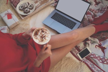 Kış tatilleri, sıcak içkiler ve insanların konsepti. Yerde kahve ve sıcak örgü battaniyeli genç bir kadın. Büyük kahve, kakao ya da kış zamanı çikolatalı Noel havası. Yumuşak odak.